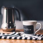 Kaffeetasse mit Kaffee, Löffel und Kaffeemaschine im Hintergrund.