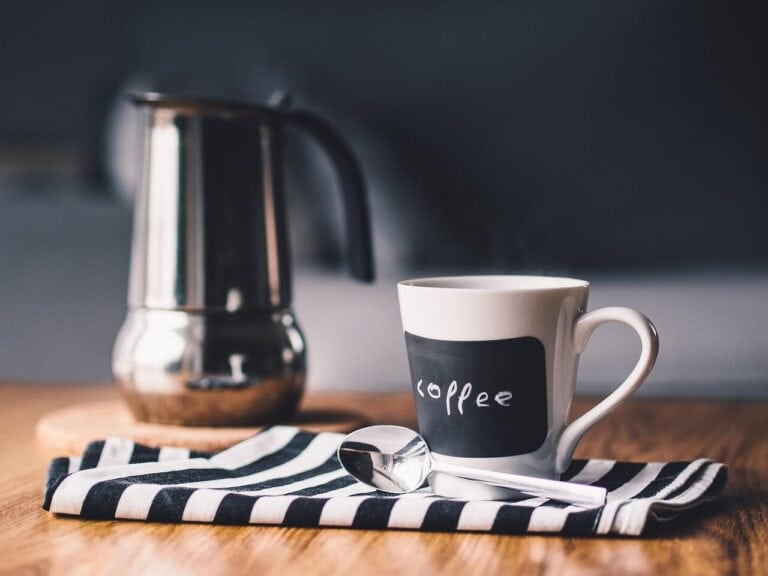 Kaffeetasse mit Kaffee, Löffel und Kaffeemaschine im Hintergrund.