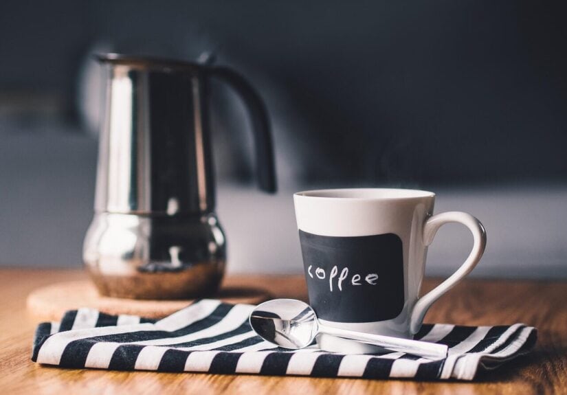 Kaffeetasse mit Kaffee, Löffel und Kaffeemaschine im Hintergrund.